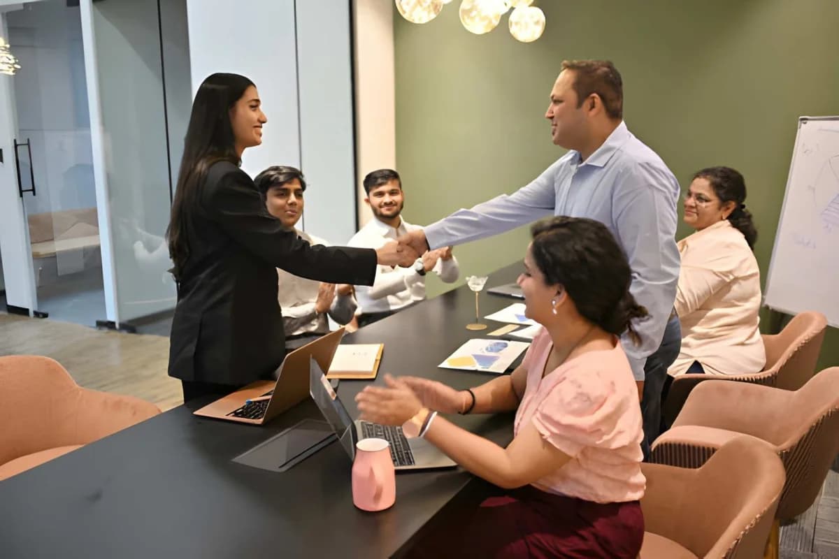 A young intern shaking hands with a mentor during a welcoming team meeting